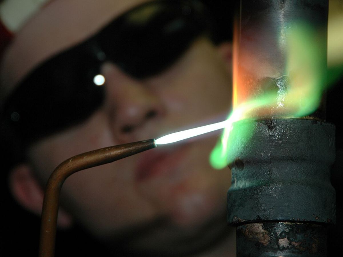Close-up of a technician brazing a copper pipe joint with a torch