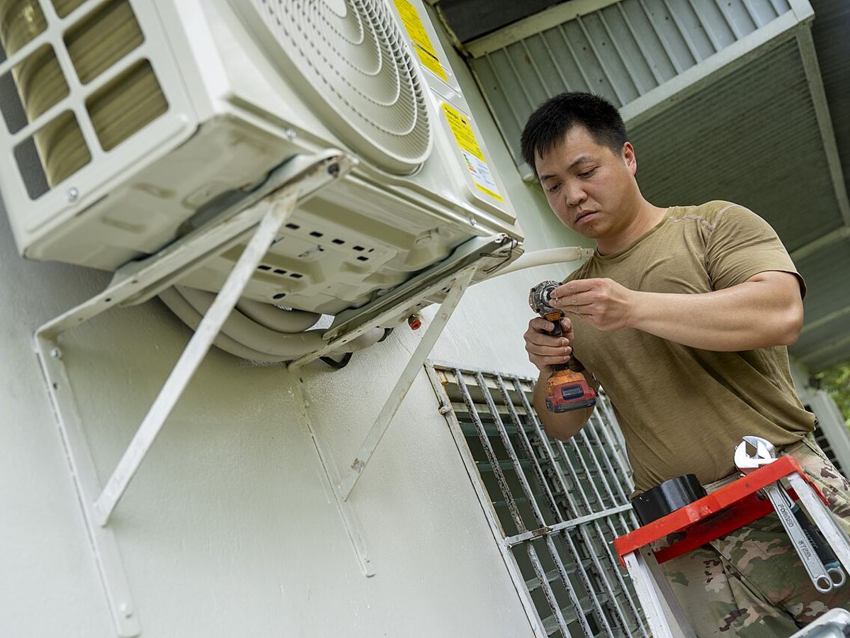 Technician working on a wall-mounted AC outdoor unit